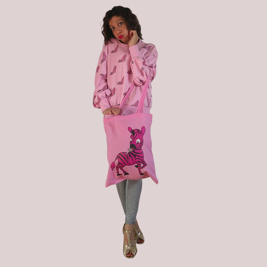 Person wearing a pink outfit with a matching bag featuring a zebra design on a plain background